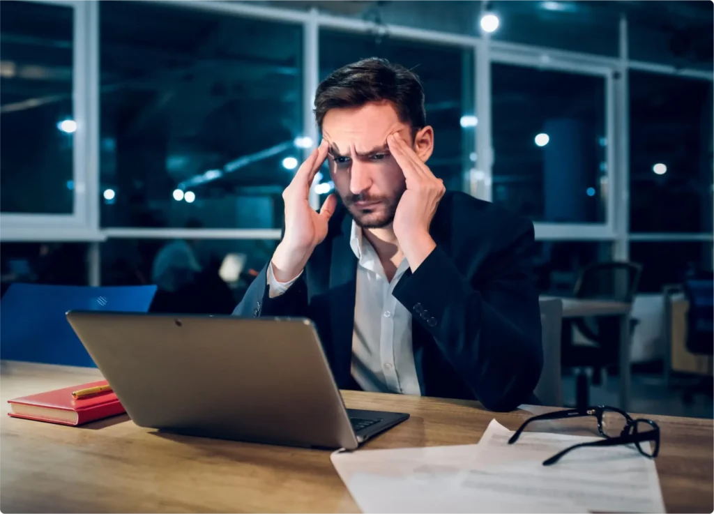 Empresário em um escritório com a mão na cabeça pensando e preocupado.